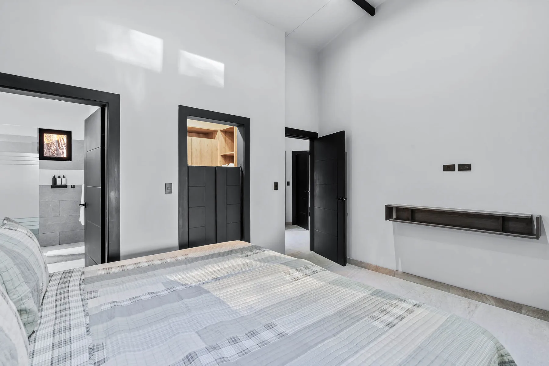 A bright bedroom with a patterned bedspread and an open doorway to a bathroom.