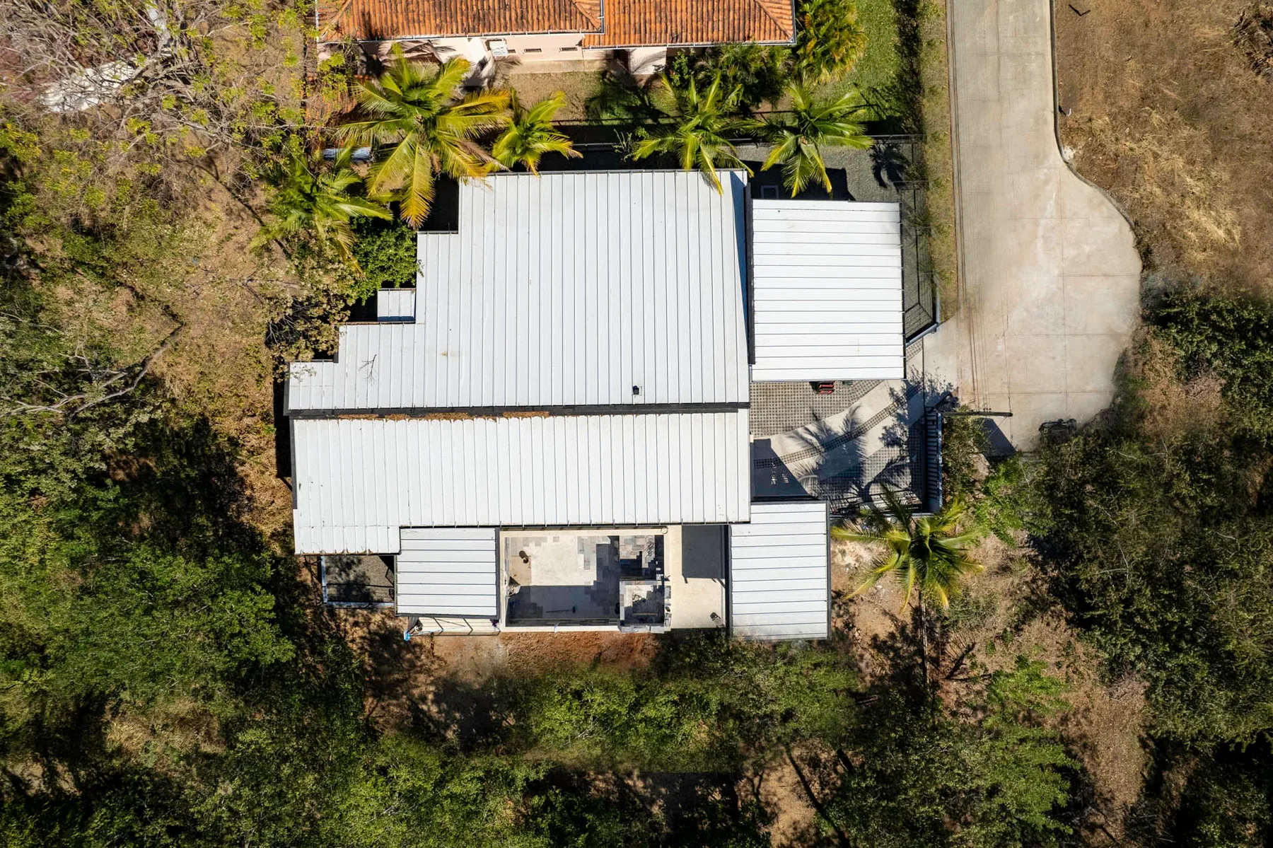 Aerial view of a building with a light-colored roof surrounded by trees.