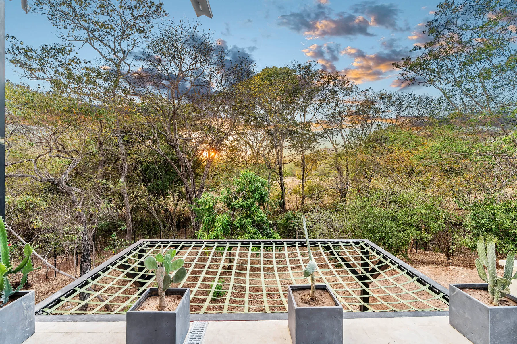An outdoor terrace overlooks a netted area and trees beneath a colorful sunset sky.