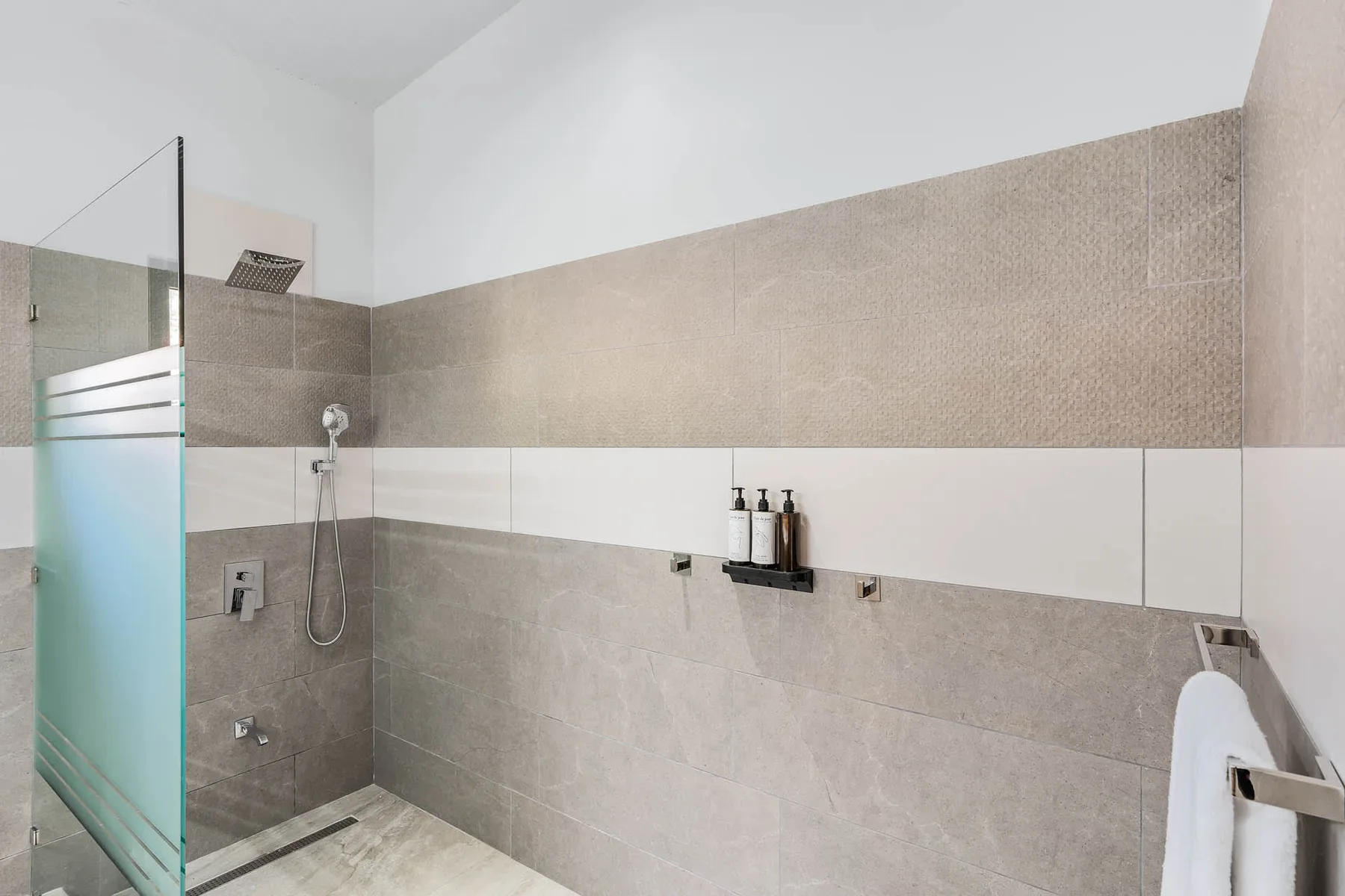 A tiled bathroom with a glass shower screen and wall-mounted fixtures.