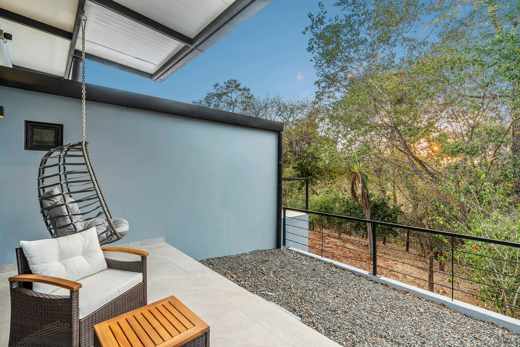 An outdoor patio with cushioned seating and a hanging chair beside a garden.