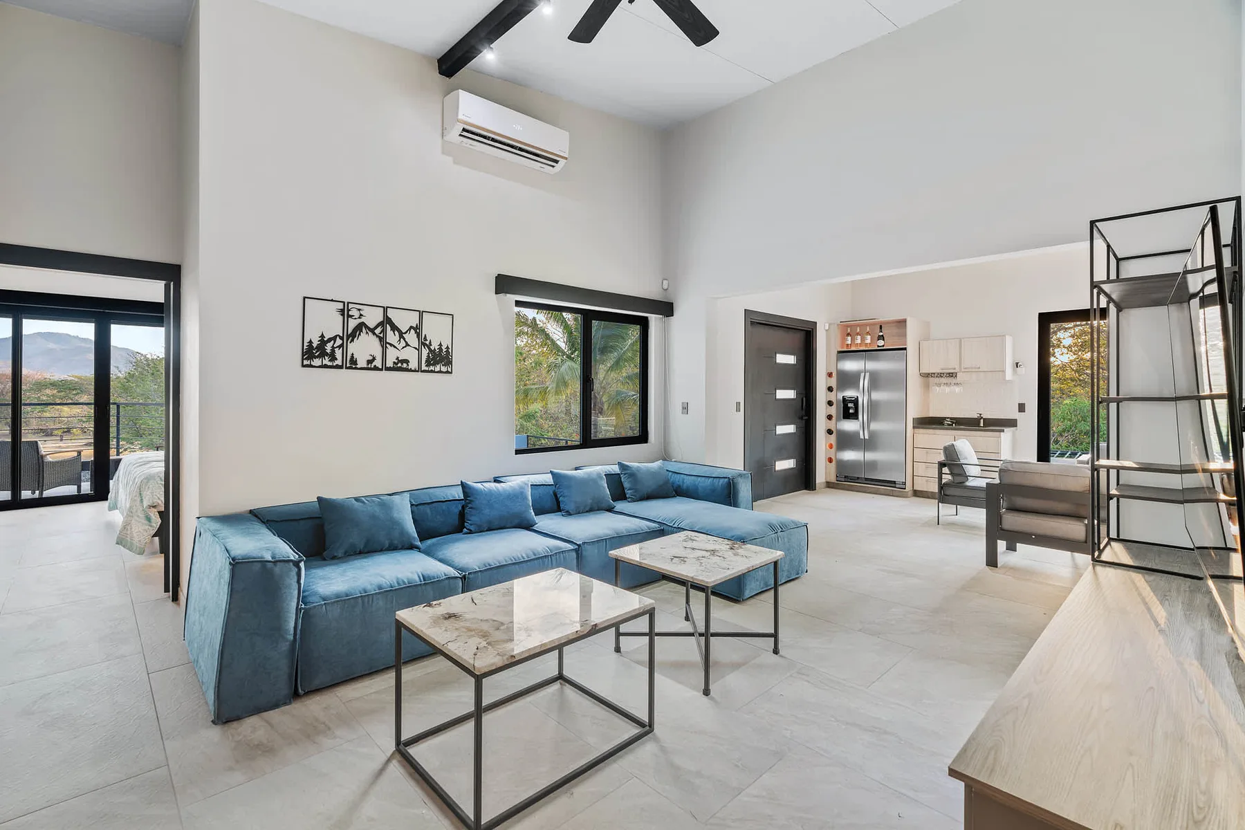 A spacious living room with blue seating and coffee tables beside an open kitchen.