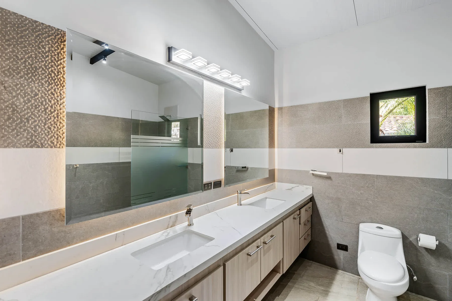 A bright bathroom with a long vanity, large mirror, and toilet.