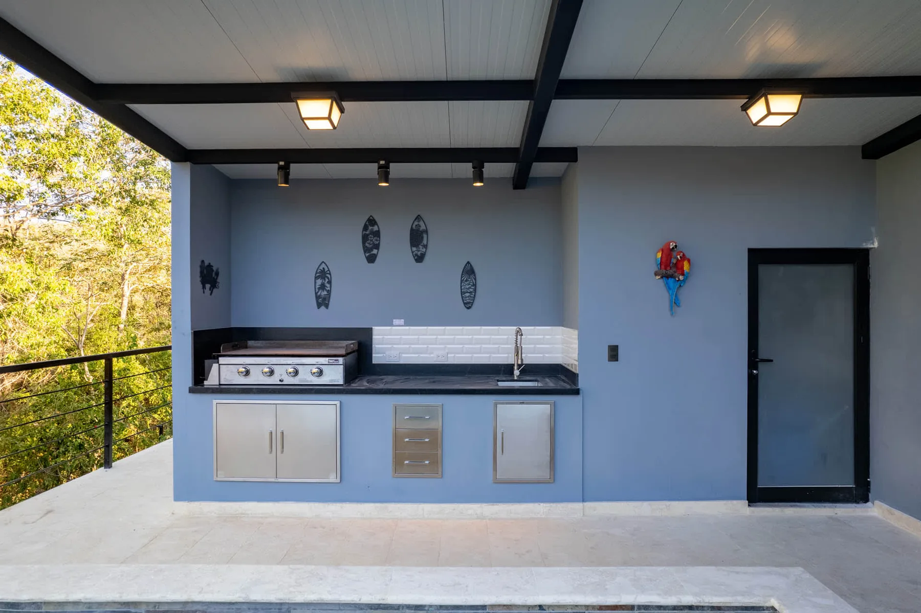 An outdoor kitchen with a counter and grill beneath a covered patio.