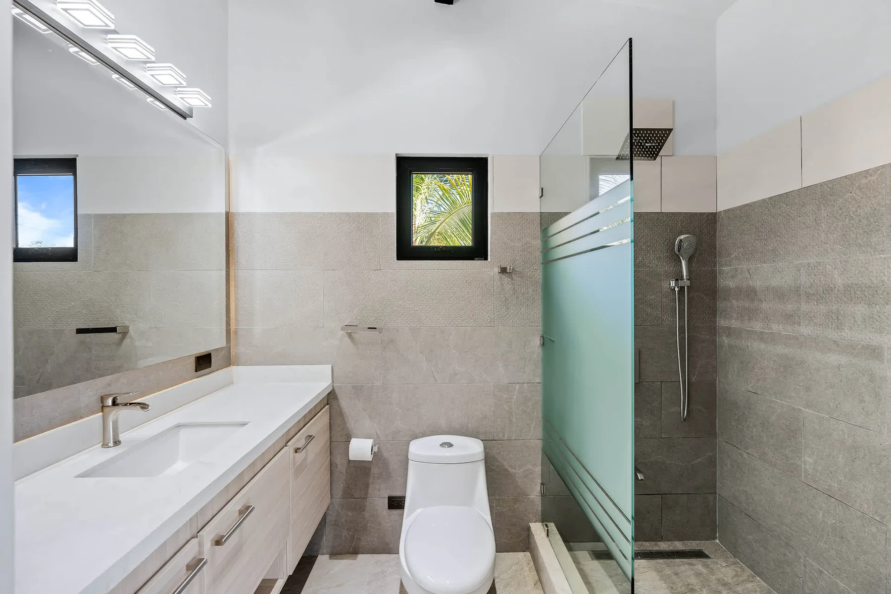 A bright bathroom with a long vanity, toilet, and glass shower.