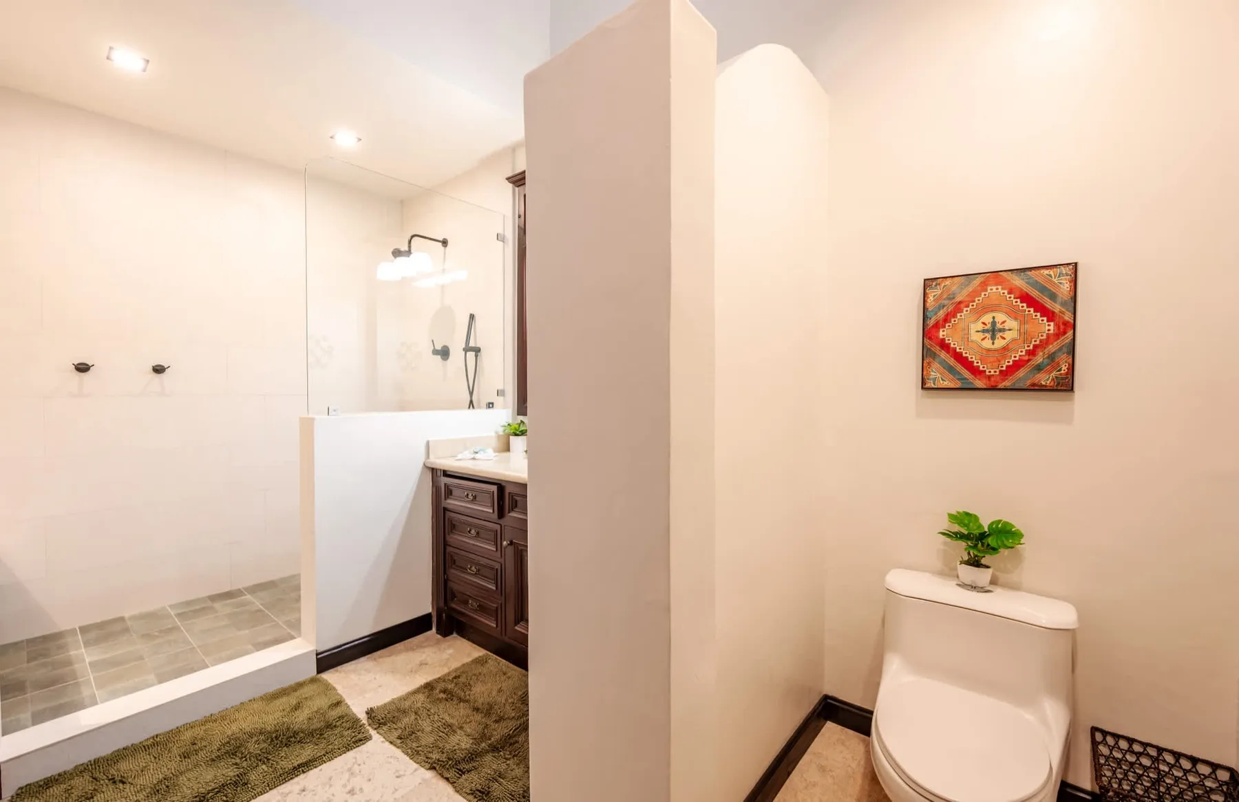 Un baño luminoso con ducha, inodoro y arte enmarcado en la pared.