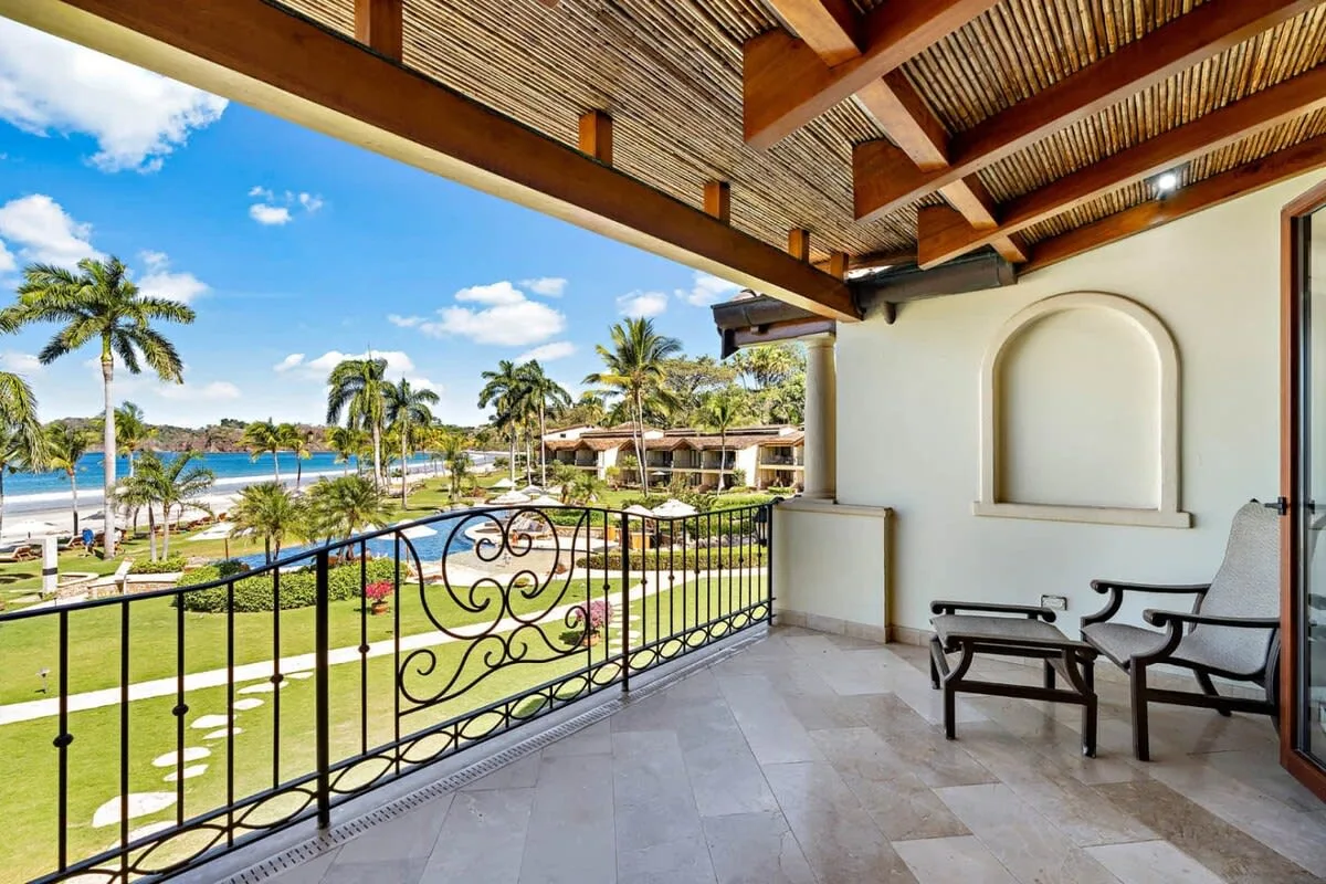 Una terraza cubierta da a un jardín, palmeras y el mar.