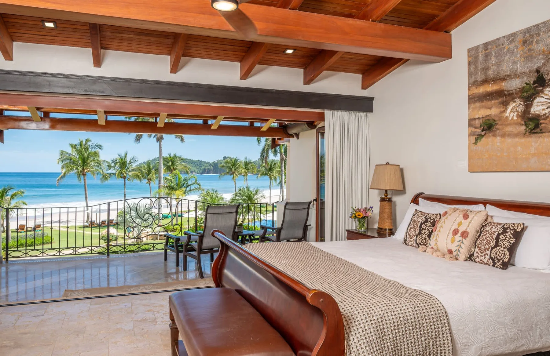 Un dormitorio da a un balcón con vistas a palmeras y al mar.