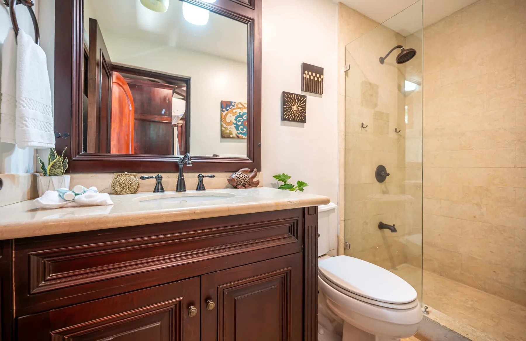 Un baño con mueble de madera oscura, espejo y ducha con mampara de vidrio.