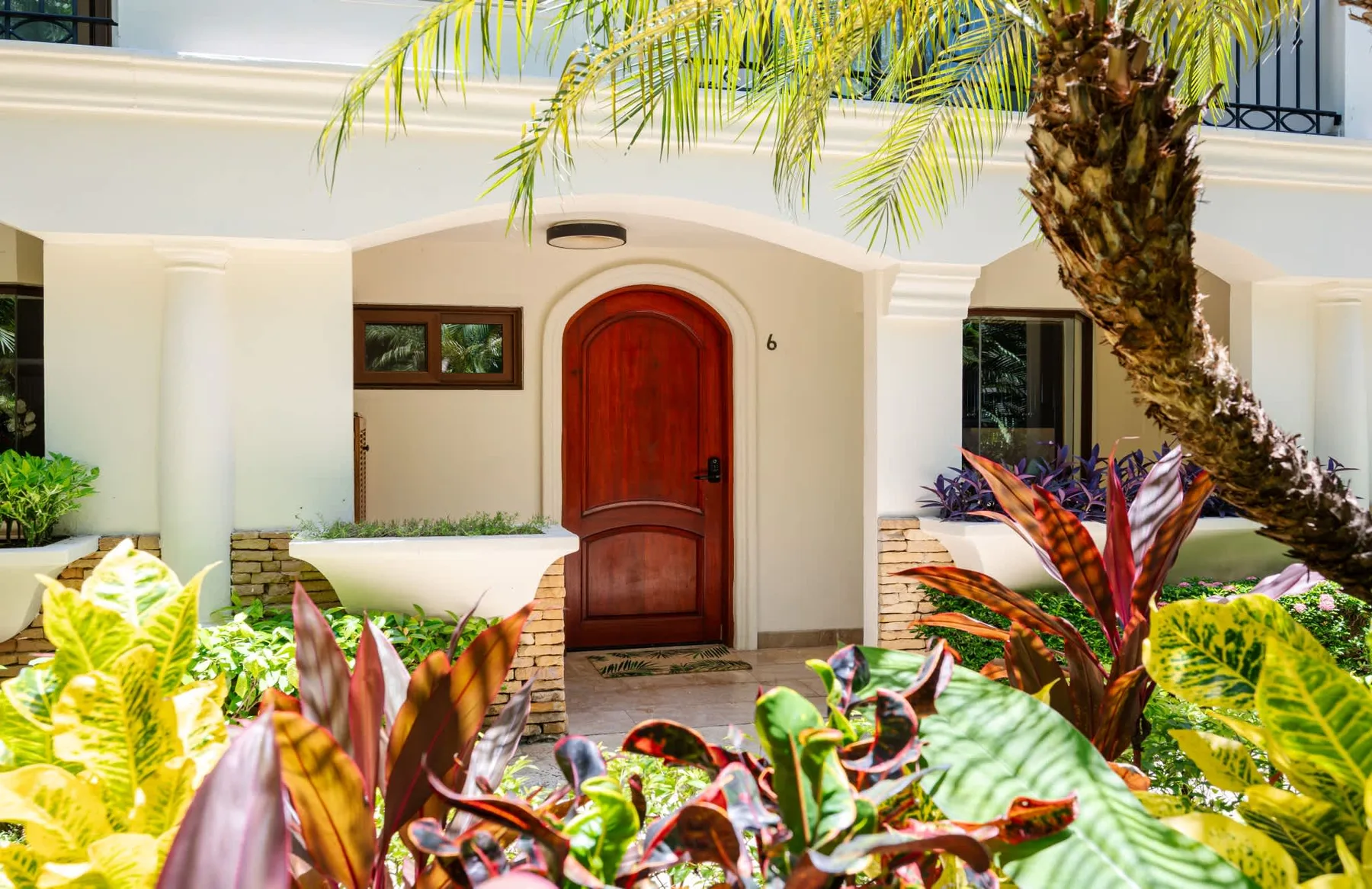 Zona común: Una entrada de casa con una puerta roja rodeada de plantas tropicales.