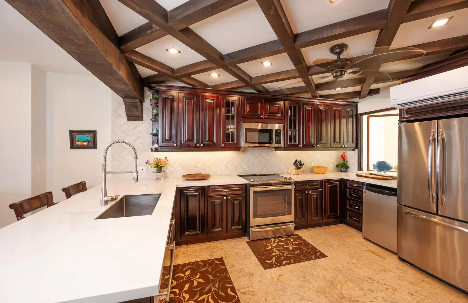 Una cocina amplia con gabinetes de madera oscura, encimeras claras y electrodomésticos de acero inoxidable.