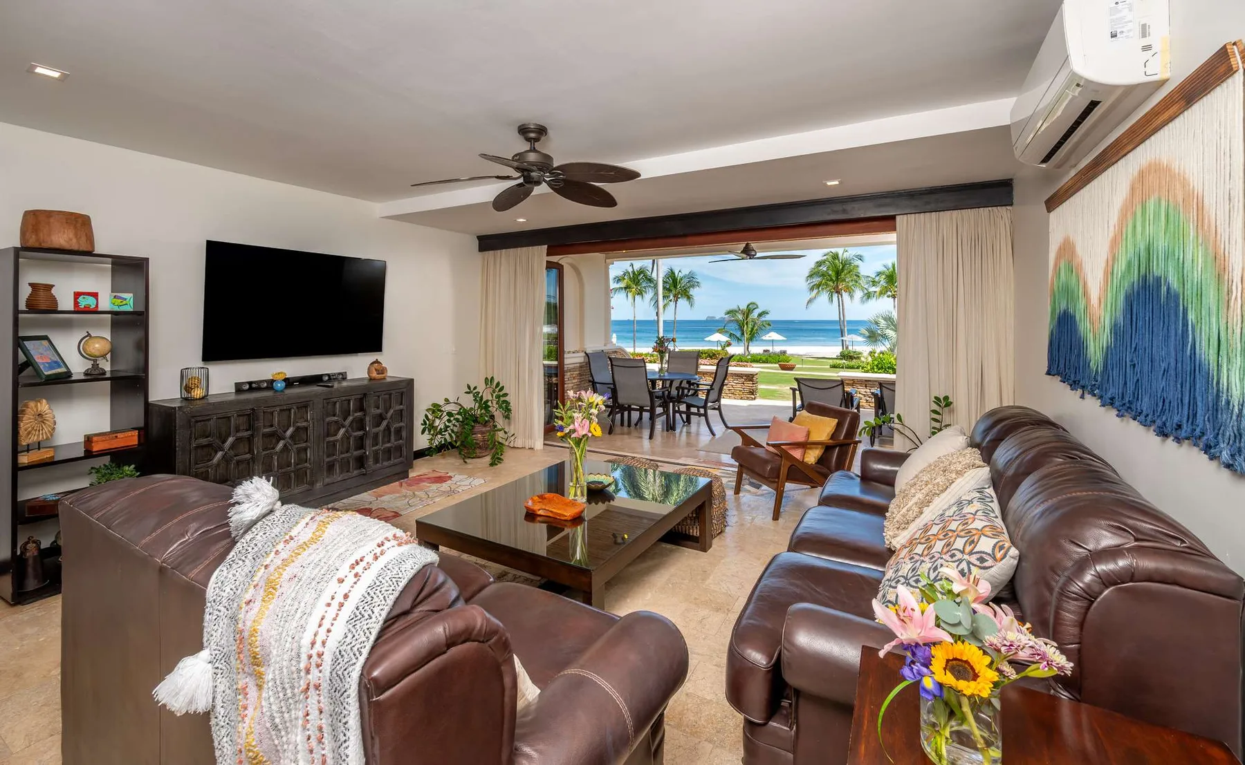 A living room with seating, a television, and an ocean view through open doors.
