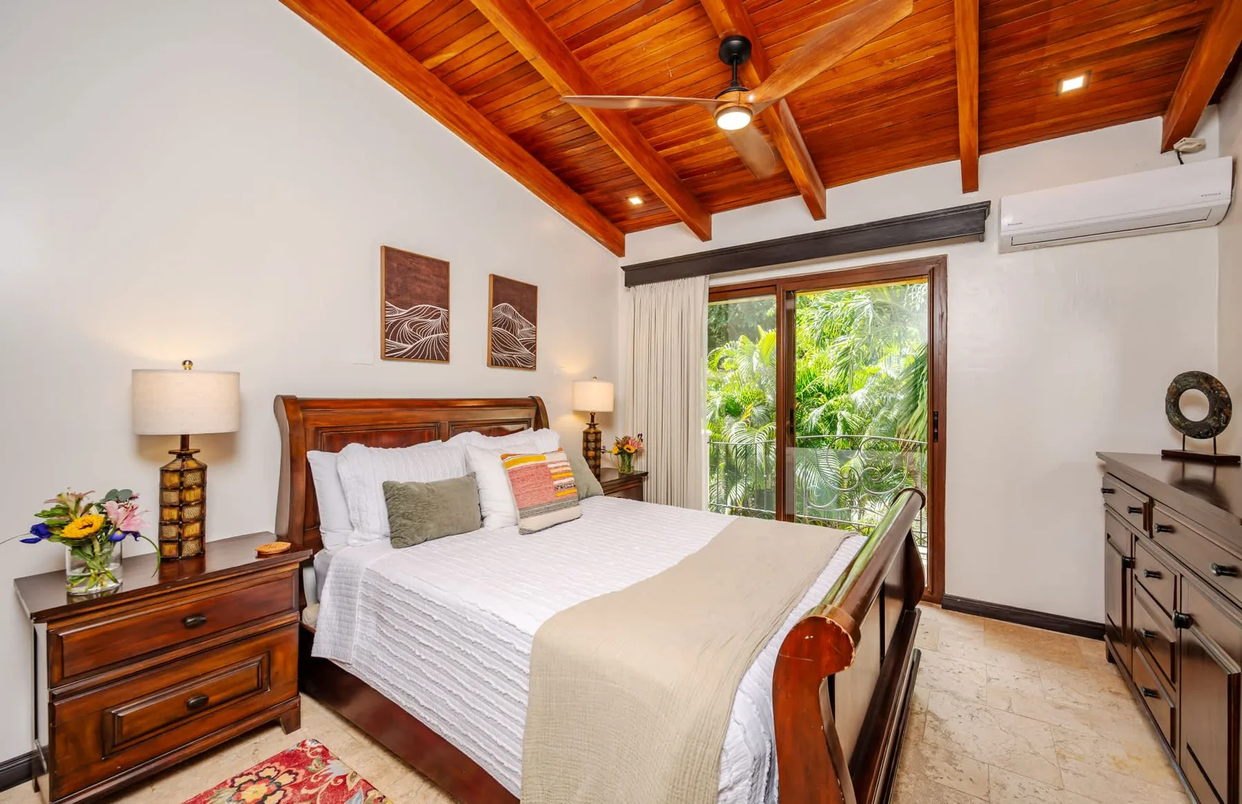 Un dormitorio con una cama de madera, ropa de cama blanca y una ventana con vegetación.