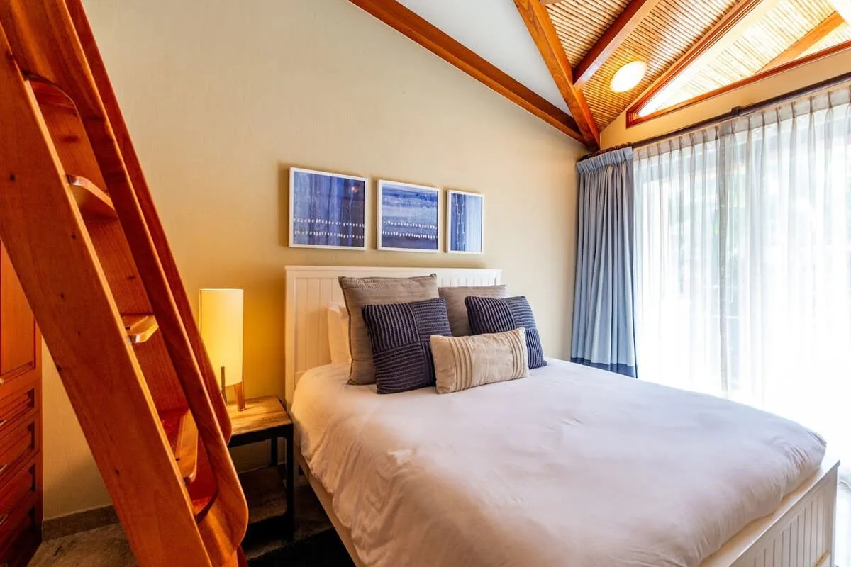 Bedroom with a bed beneath a sloped ceiling and large curtained windows.