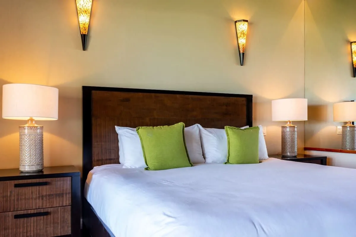 A bedroom with a neatly made bed and green accent pillows.