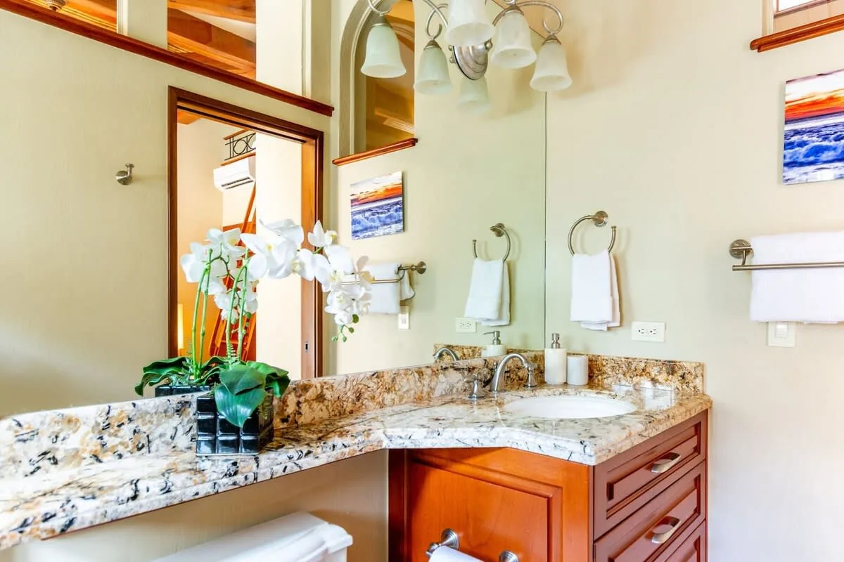 A bathroom vanity with a large mirror and flowers on the counter.