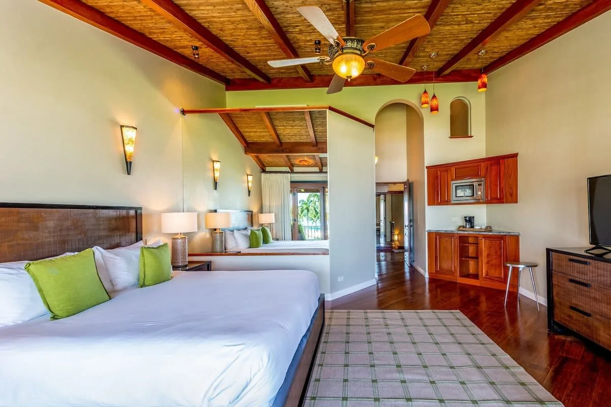 A bedroom with a large bed, a kitchenette, and a television.