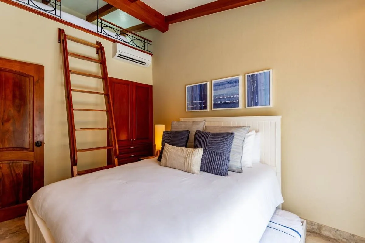 A bedroom with a bed, decorative pillows, and framed artwork above the headboard.