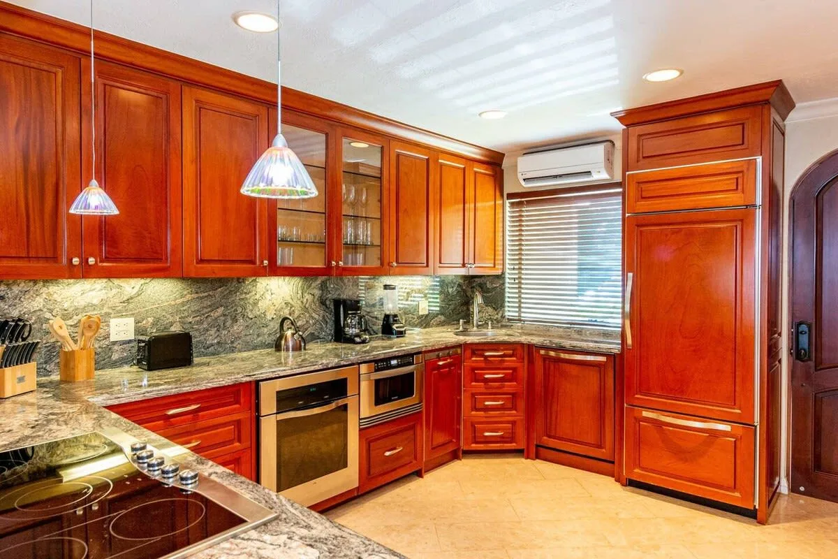 A kitchen with reddish wood cabinets, granite counters, and a cooking area.