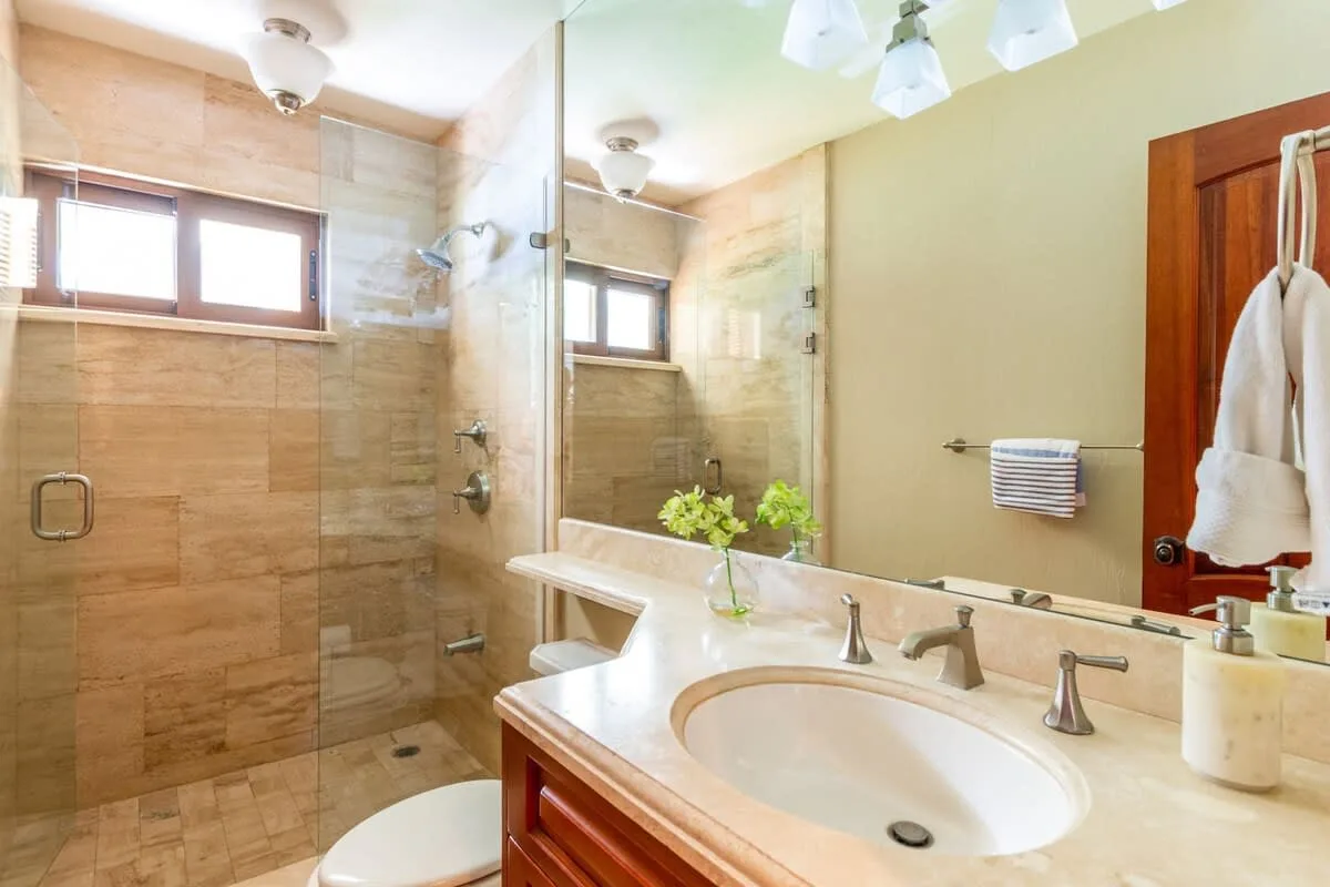 A bathroom with a glass shower, a sink, and a large mirror.
