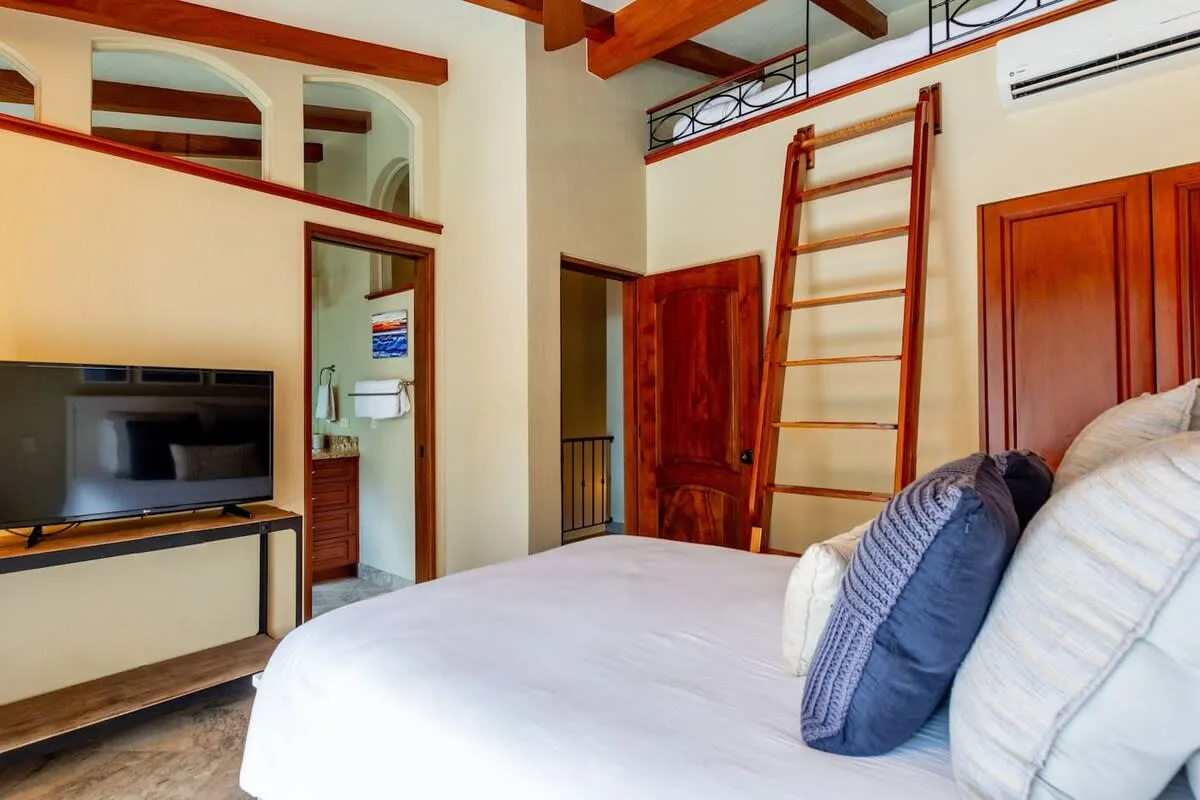 A bedroom with a bed, television, and wooden ladder leading to a loft.