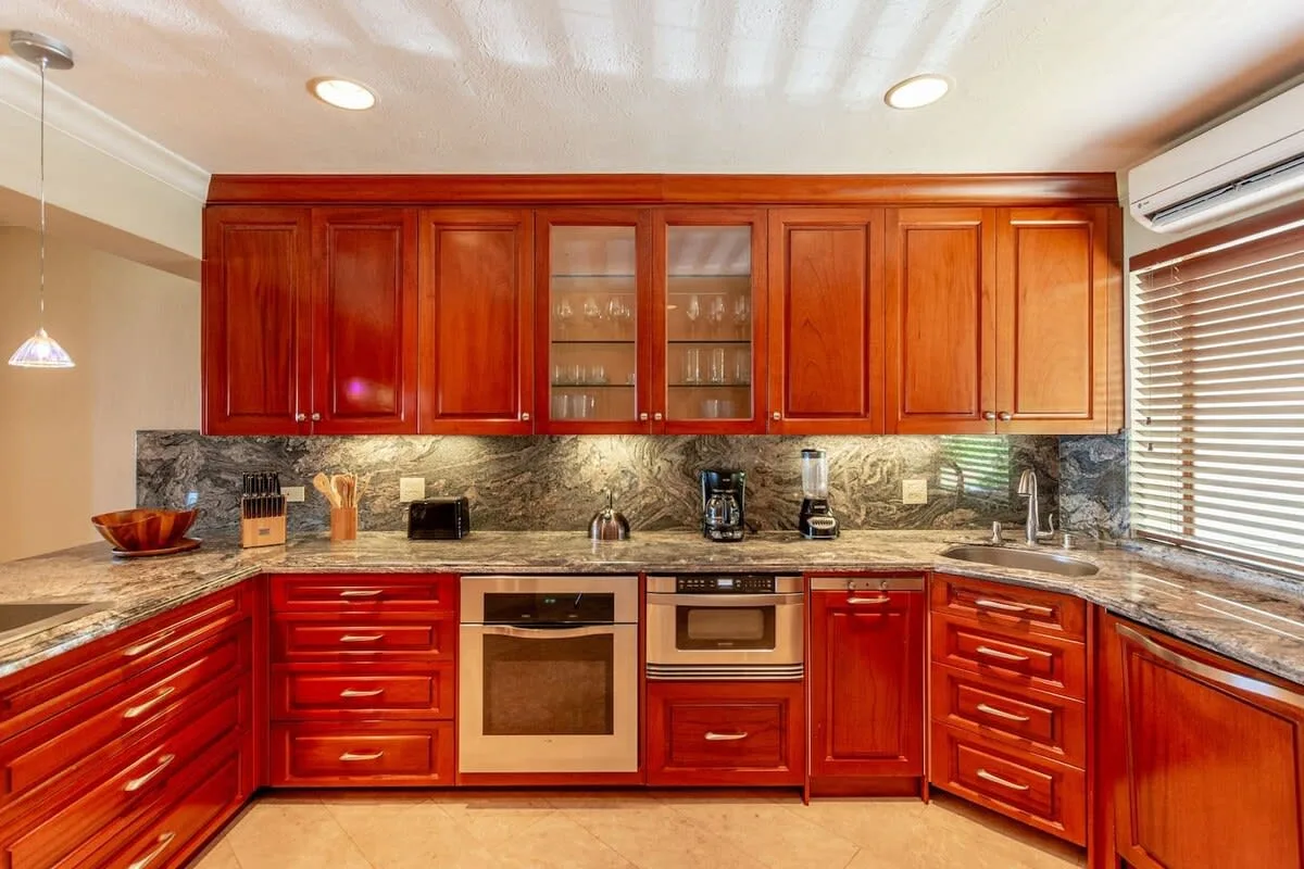 A kitchen with reddish wood cabinets, stone counters, and built-in appliances.