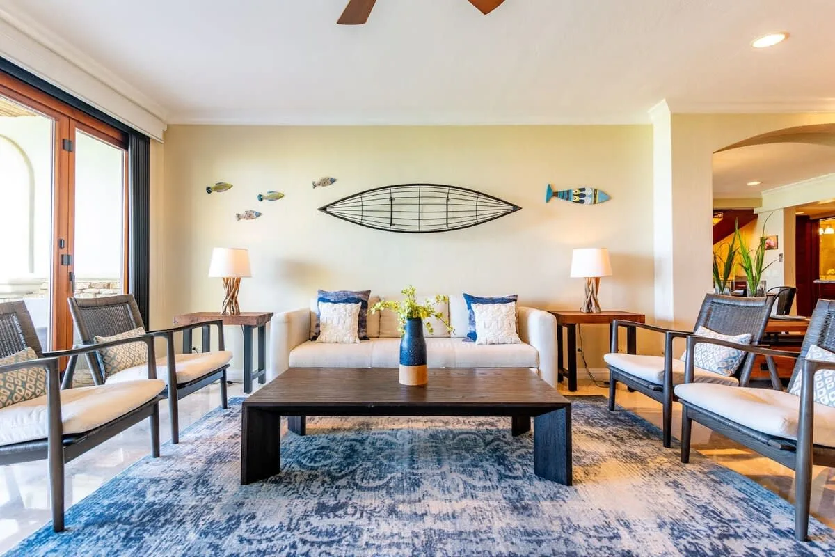 A bright living room has seating around a coffee table beneath fish-shaped wall decor.