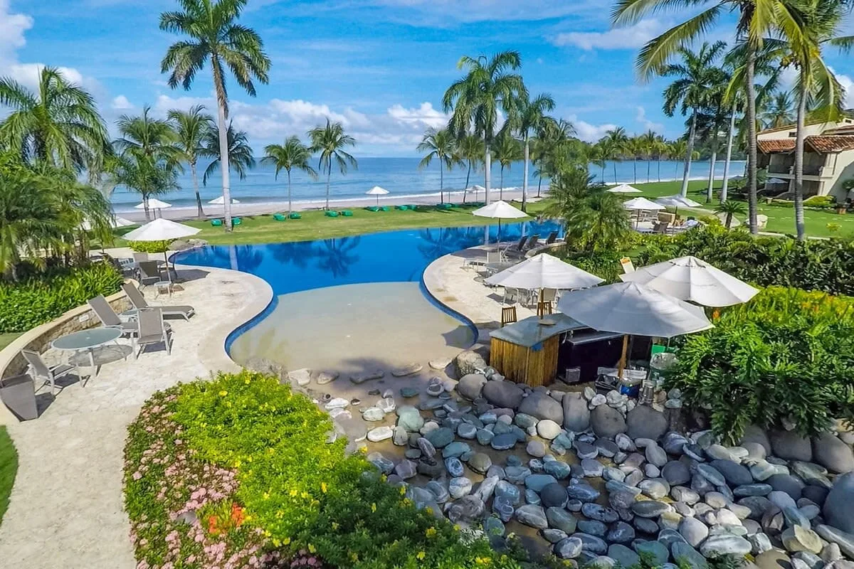 Shared amenity: A resort pool beside a landscaped garden, with palm trees and the ocean beyond.