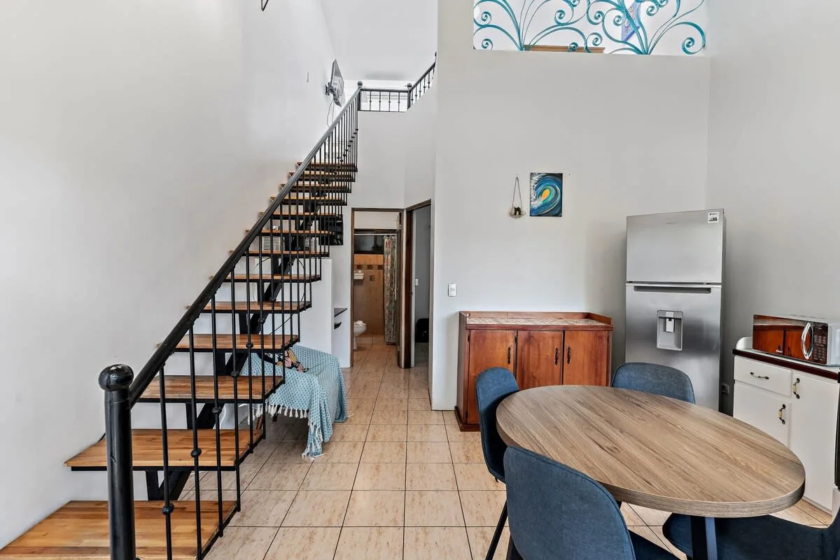 A dining area with a wooden table, beside a staircase and kitchen appliances.