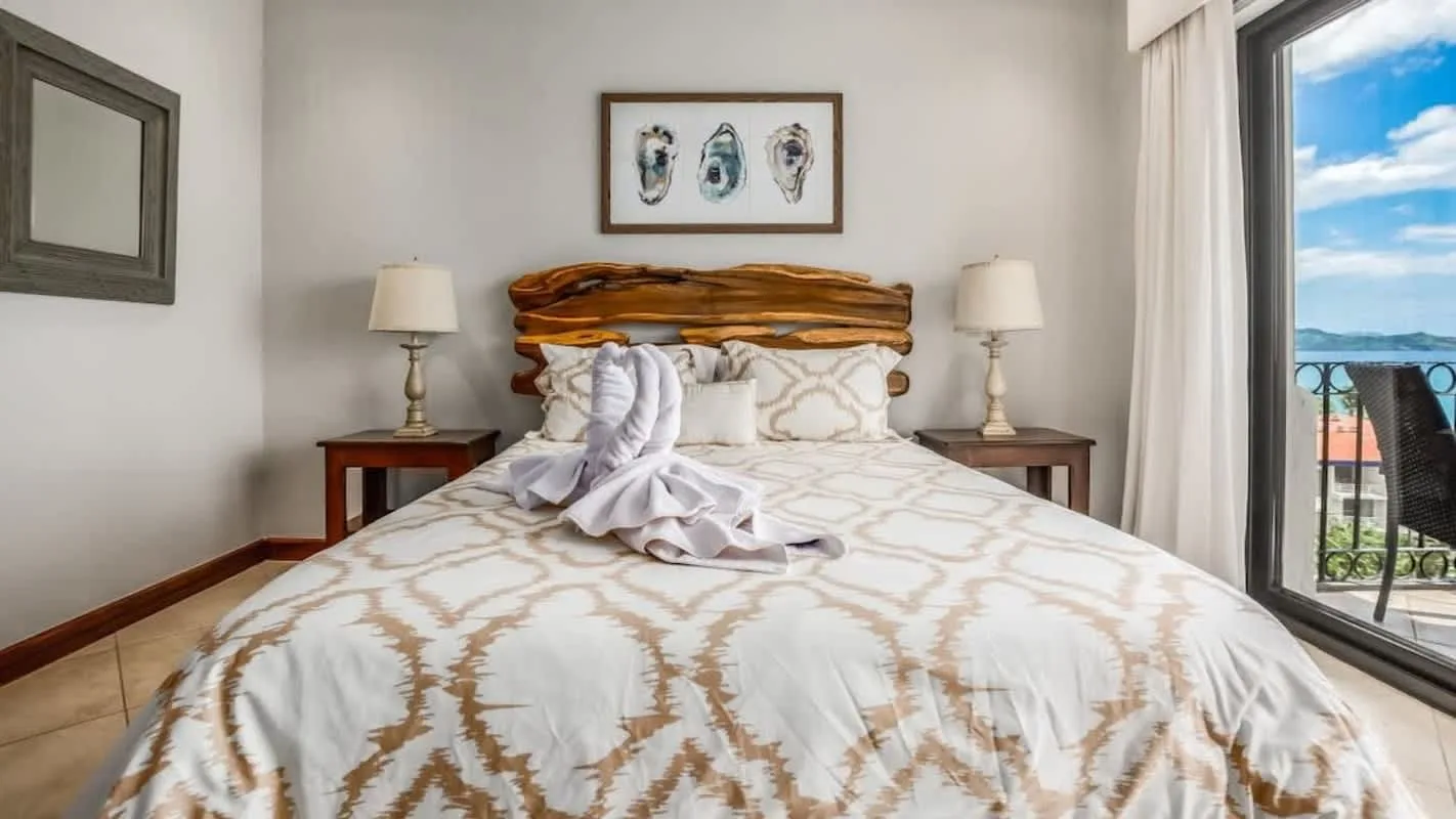 A bedroom with a large bed, matching bedside tables, and a window overlooking the water.