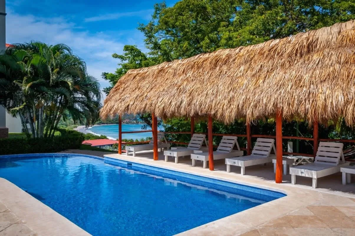 Shared amenity: Outdoor pool beside a thatched-roof seating area.