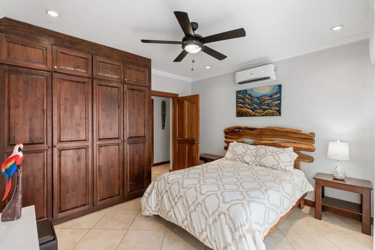 A bedroom with a bed, dark wood cabinets, and a ceiling fan.