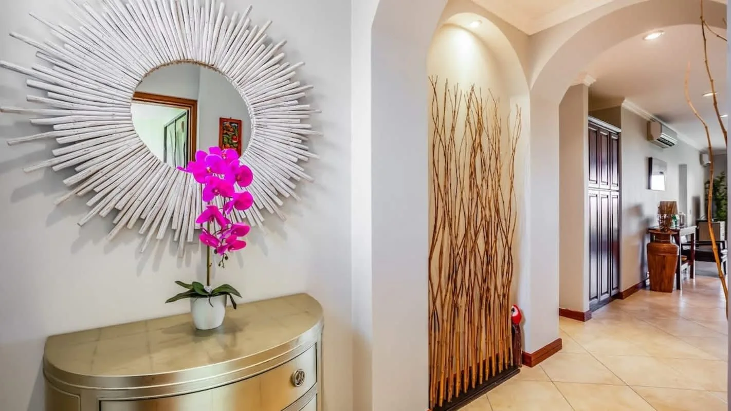 An entryway features a round decorative mirror, a console table, and a potted orchid.