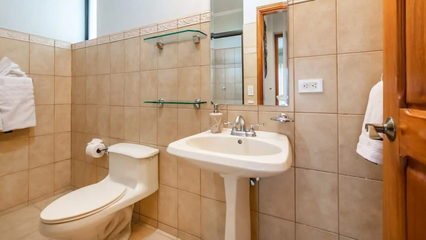 A tiled bathroom with a sink, toilet, and mirror.