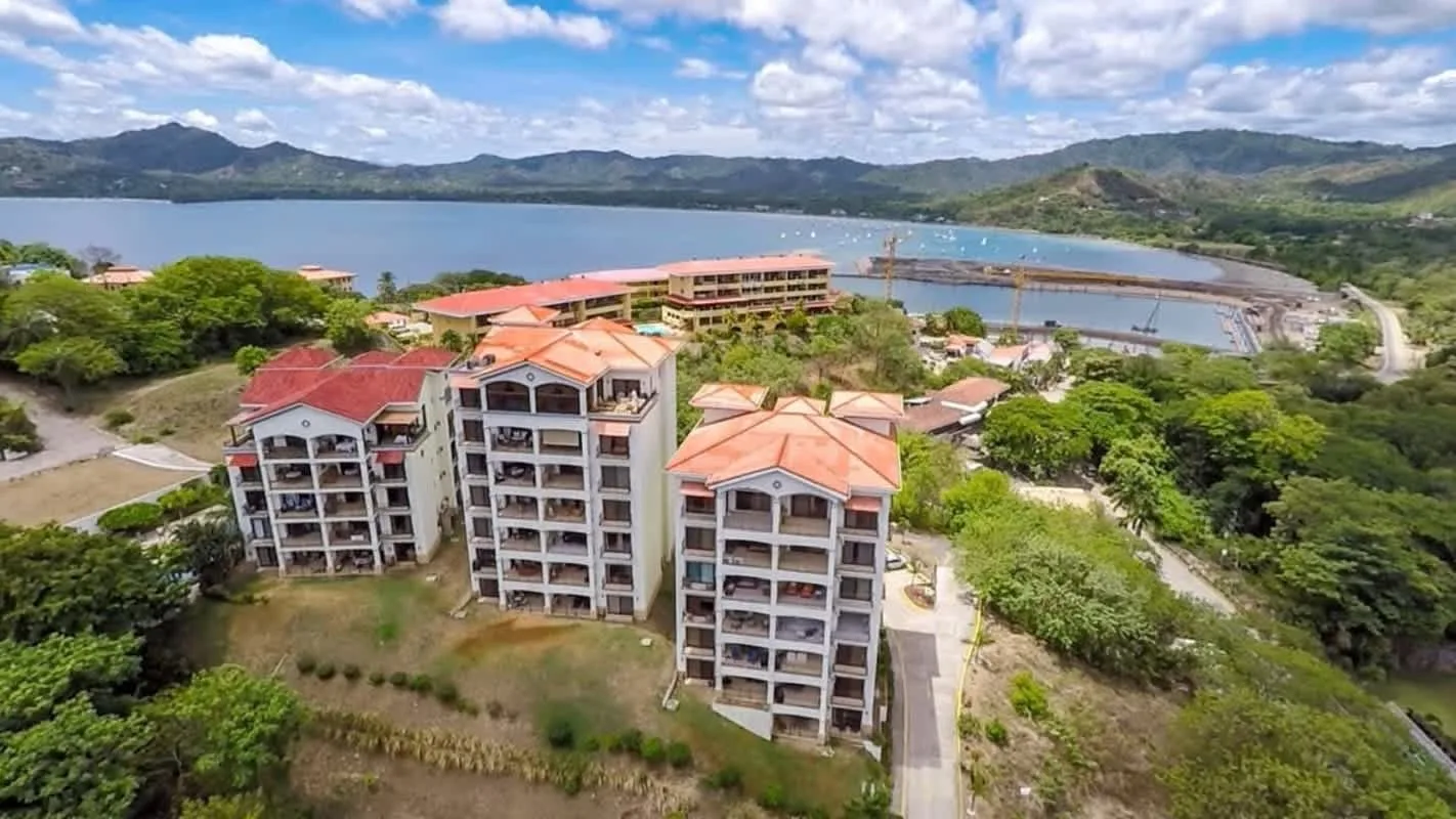 Shared amenity: Aerial view of several buildings beside a lake and surrounding hills.