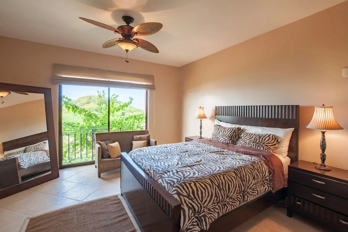 A bedroom with a patterned bed and a window overlooking green trees.