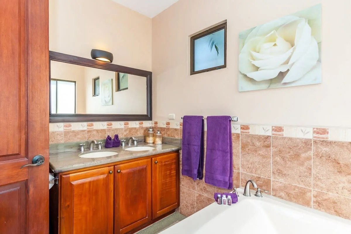 A bathroom vanity with a wide mirror, purple towels, and a bathtub.