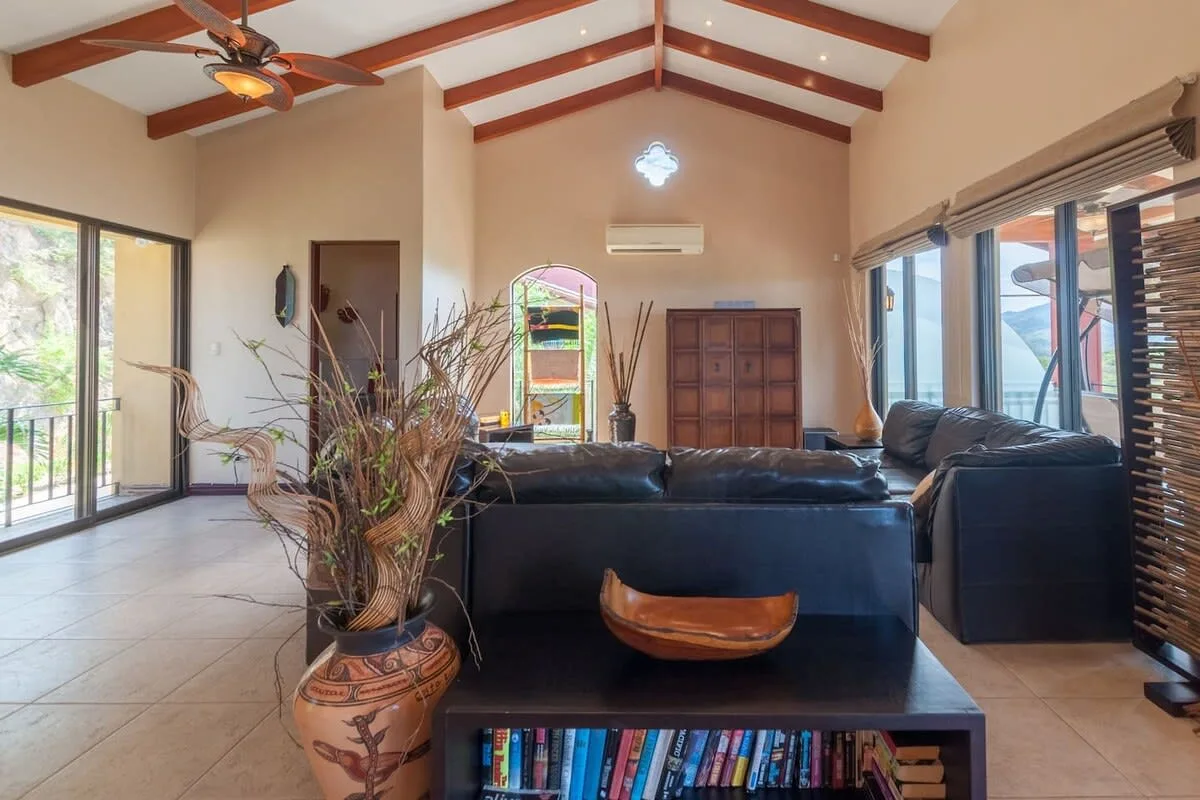 A living room with dark seating, a low table, and large windows.
