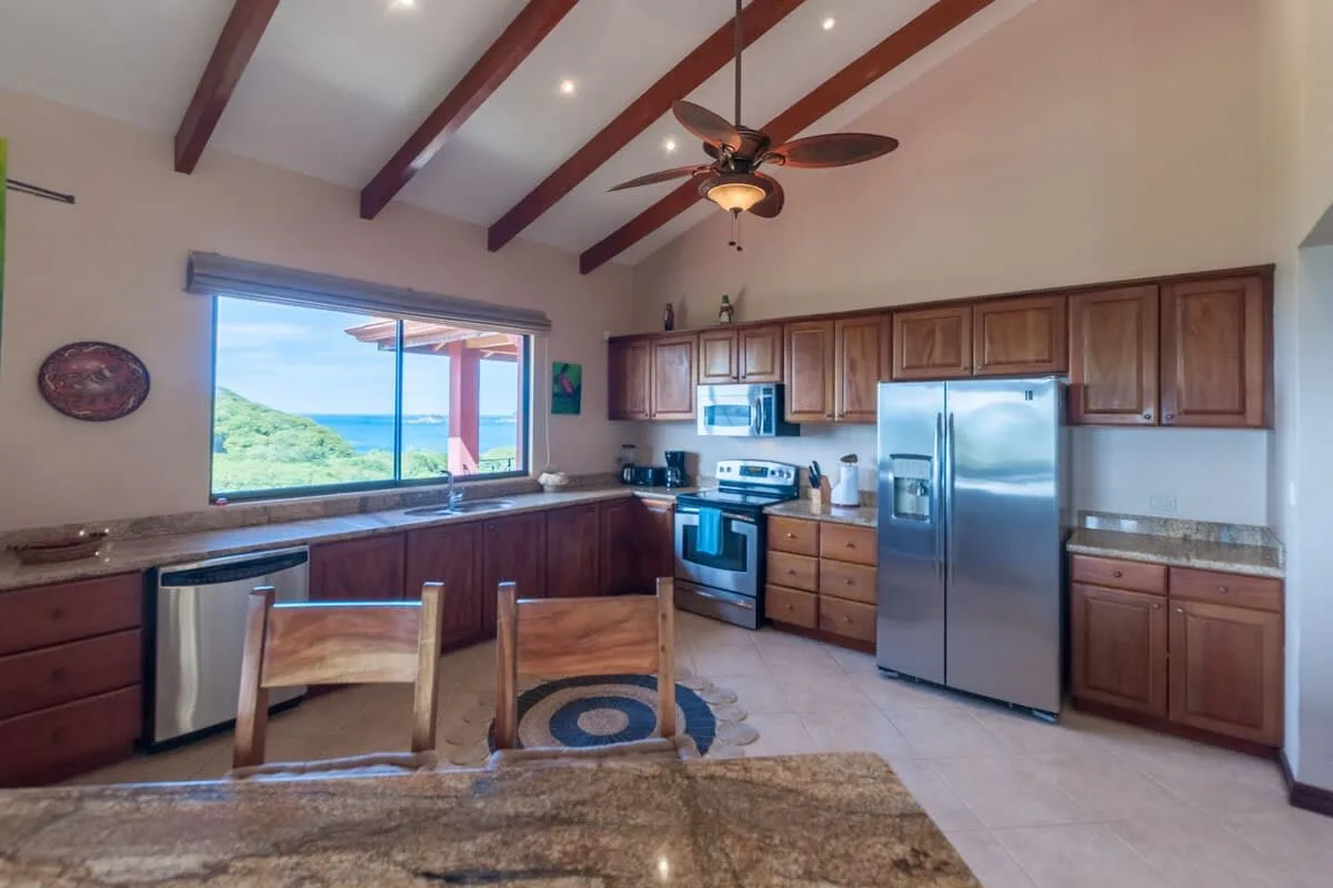 A spacious kitchen with wooden cabinets, stainless steel appliances, and a window overlooking greenery.