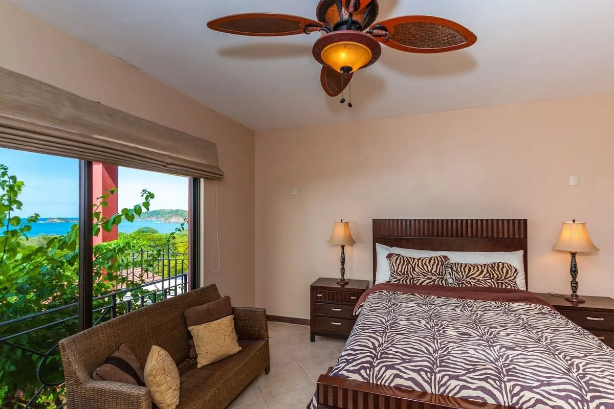 A bedroom with a patterned bed and a seating area beside a large window.