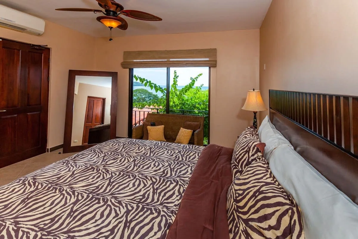 A bedroom with a patterned bedspread and a window overlooking greenery.