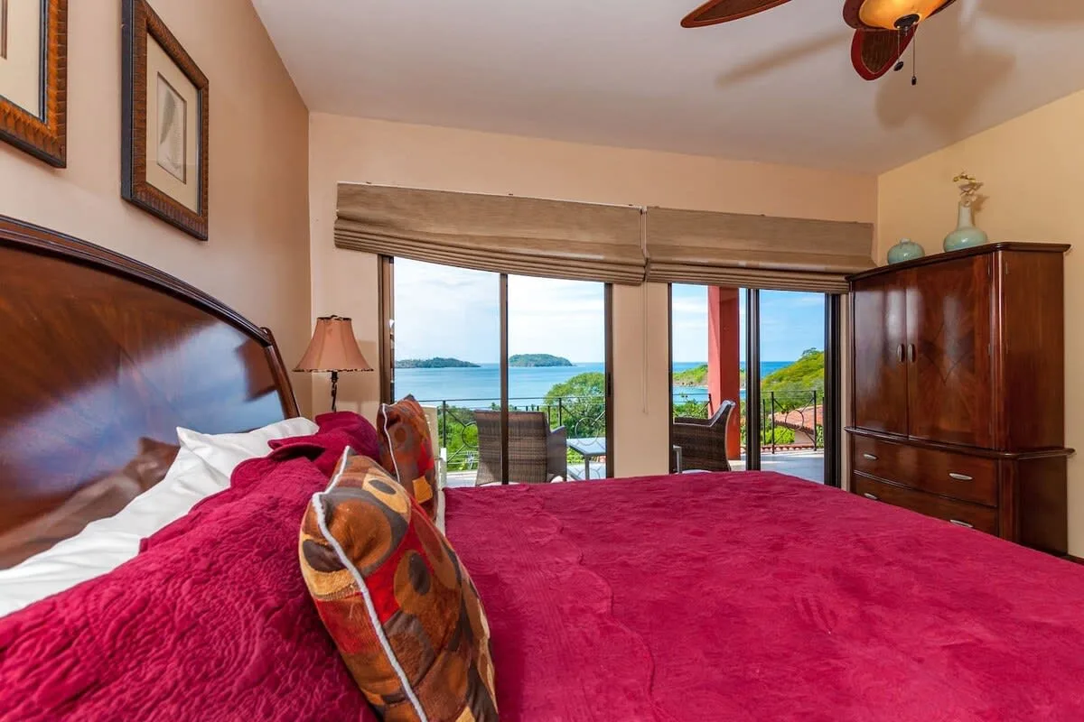 A bedroom with a bed facing large windows overlooking the water.
