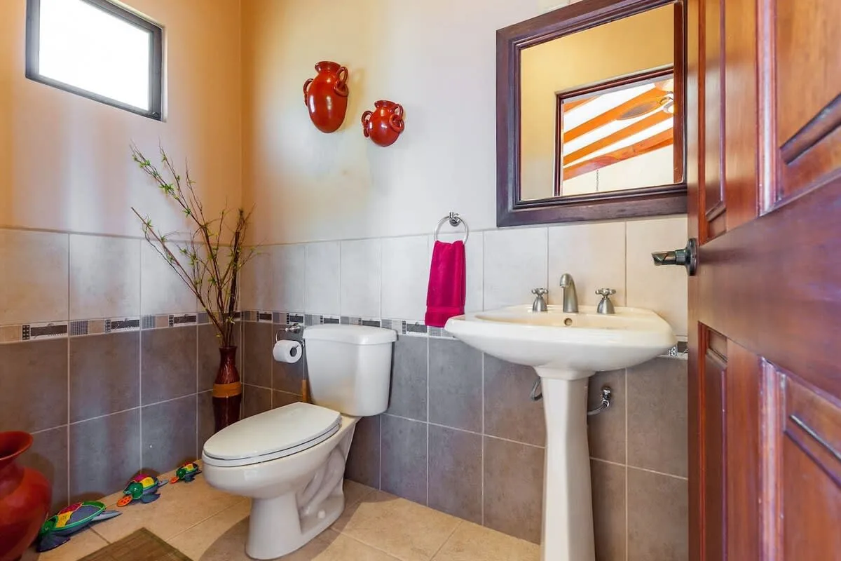 A bathroom with a pedestal sink, toilet, and tiled walls.