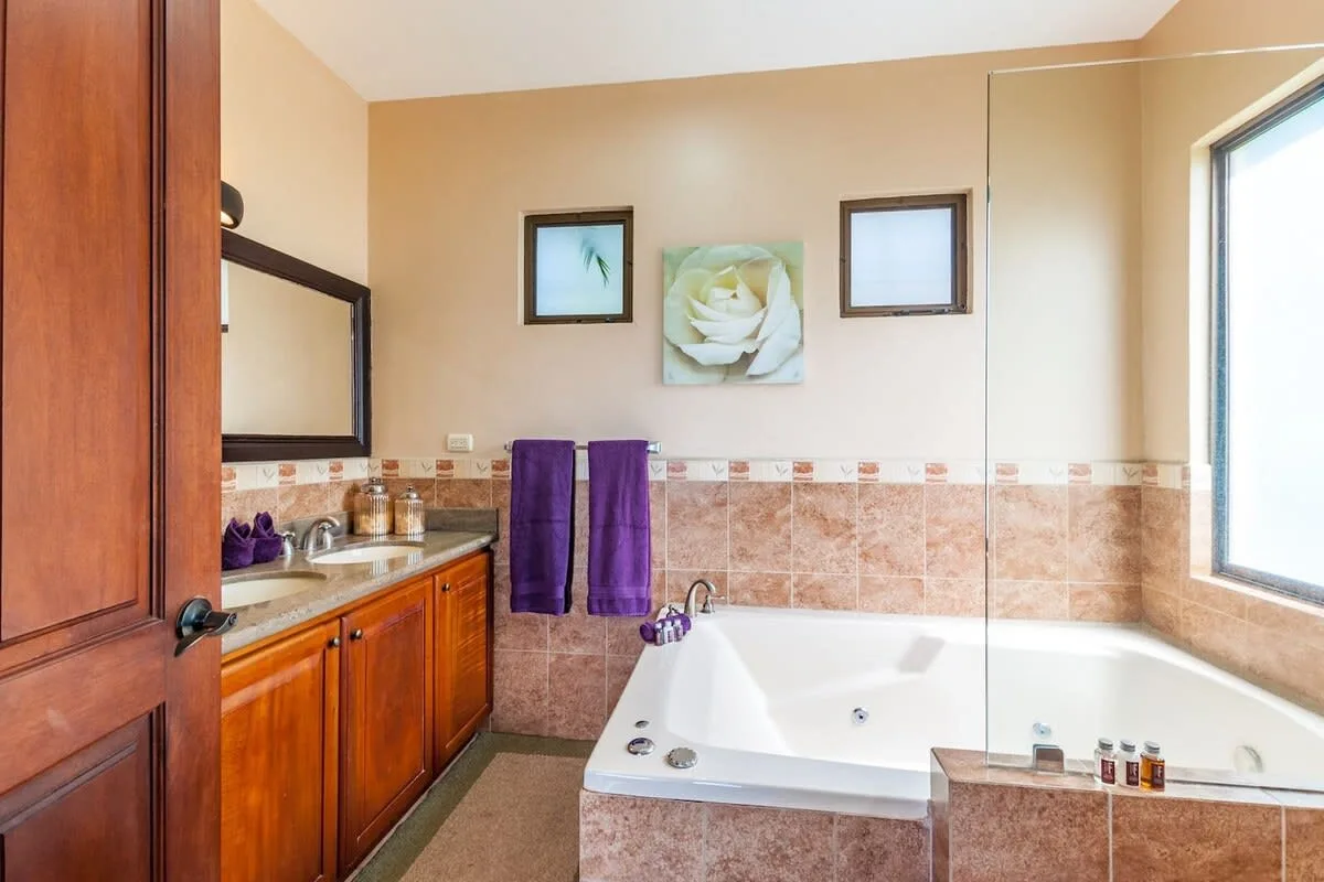 A bathroom with a built-in bathtub, wooden vanity, and purple towels.