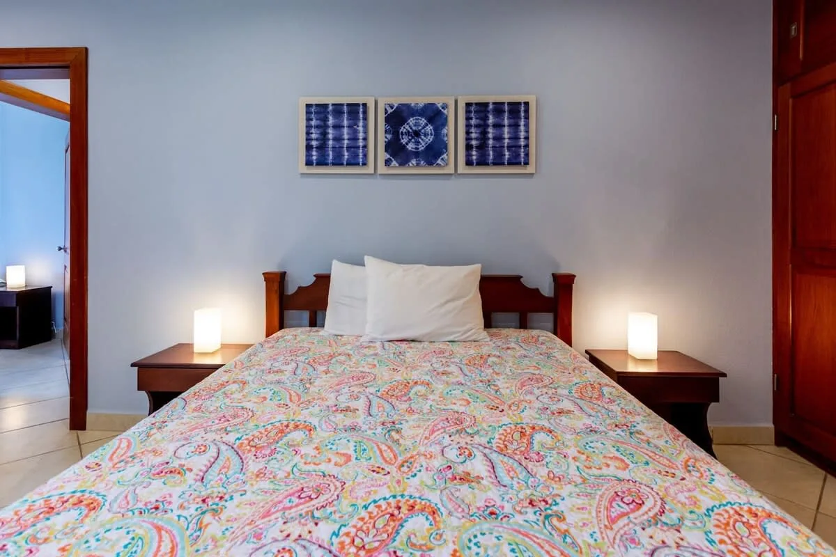 A bedroom with a wooden bed, patterned bedding, and framed artwork above it.