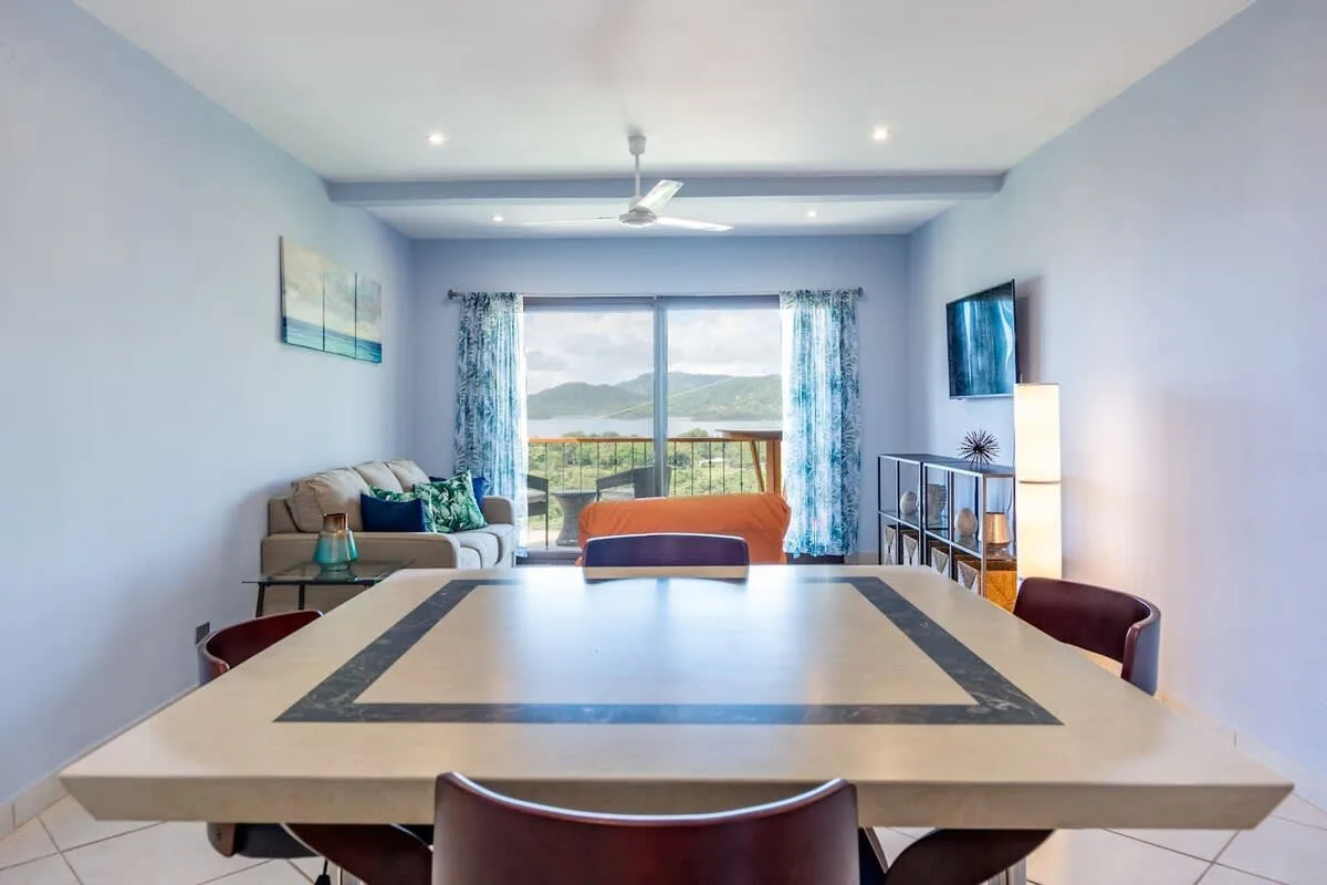 A bright living and dining area with a large table facing sliding glass doors.