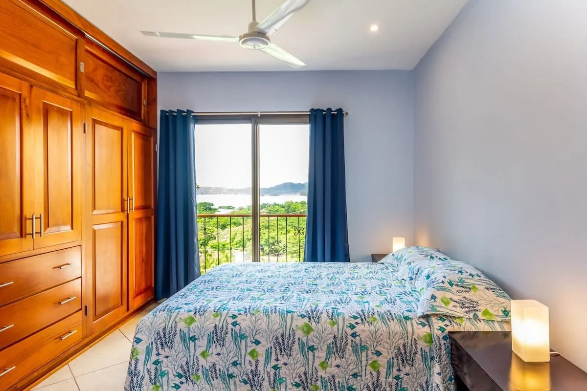 A bedroom with a patterned bedspread and blue curtains beside a window.