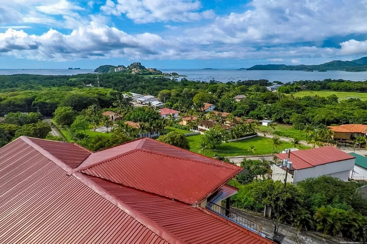 Shared amenity: Aerial view of red-roofed buildings among green trees, with water in the distance.