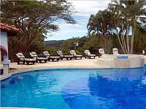 Una piscina al aire libre está junto a una terraza pavimentada con asientos y palmeras.