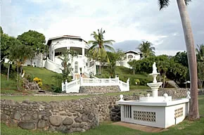 Un jardín ajardinado rodea un edificio blanco con una terraza elevada.
